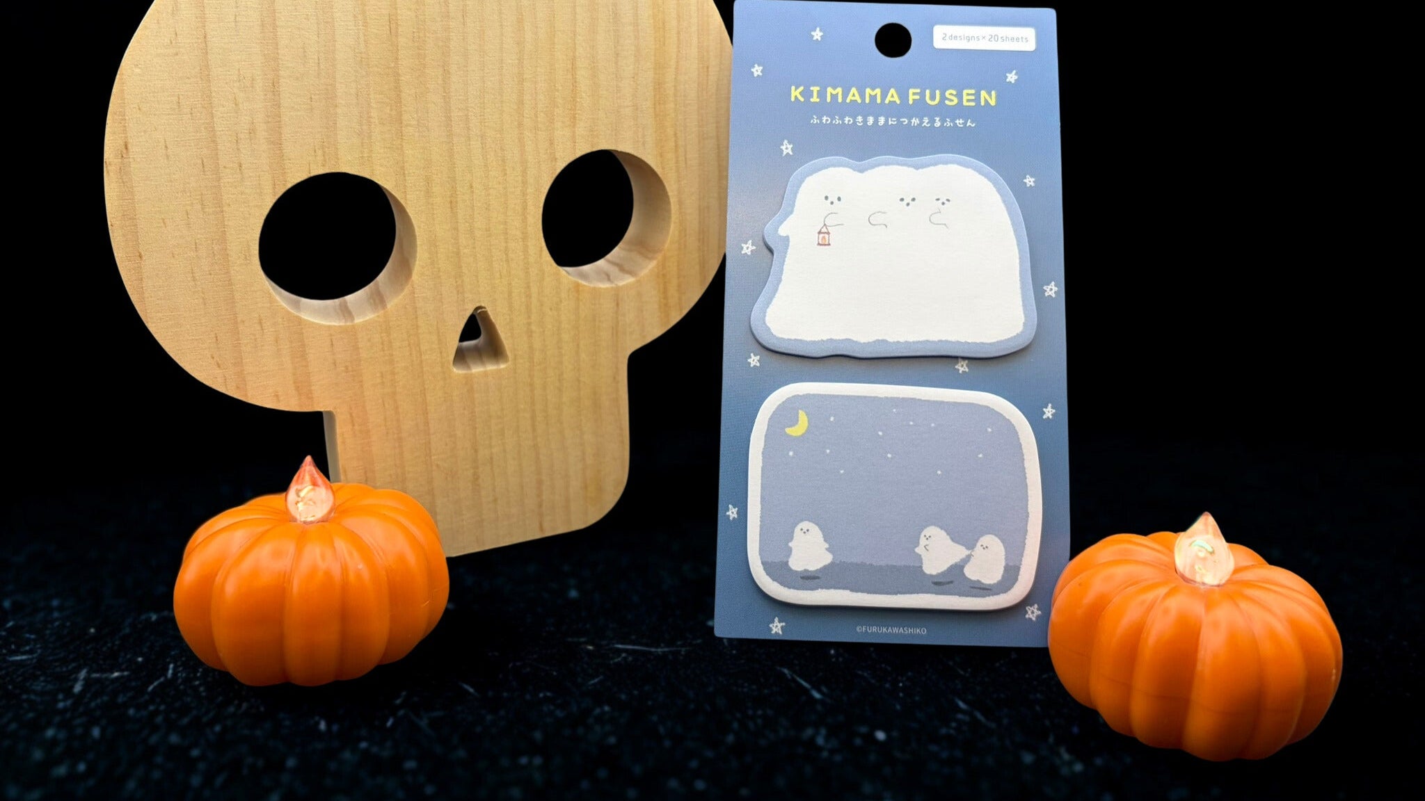 Wooden skull with small pumpkins on a dark background and ghost sticky notes