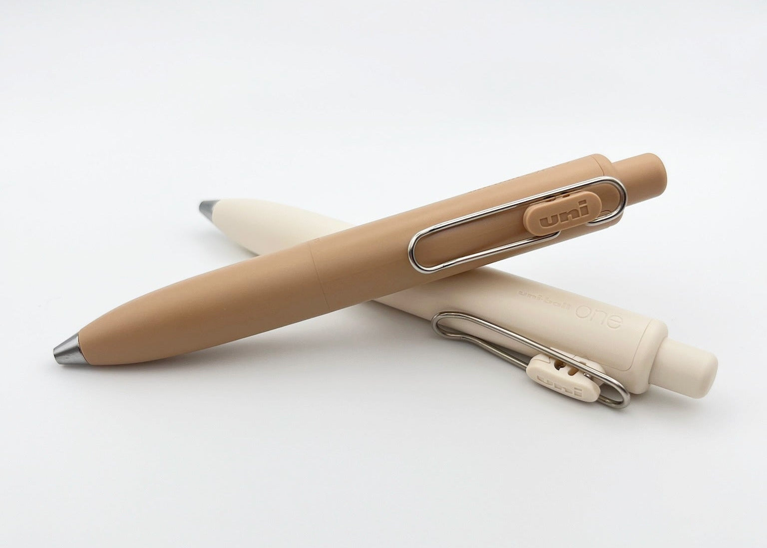 Two pens, one beige and one white, on a light gray background